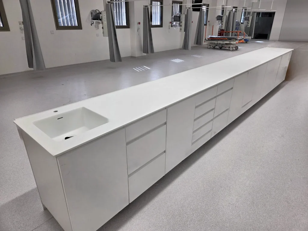 Encimera corrida de solid surface blanco con lavabo integrado sobre módulos con cajoneras en un hospital