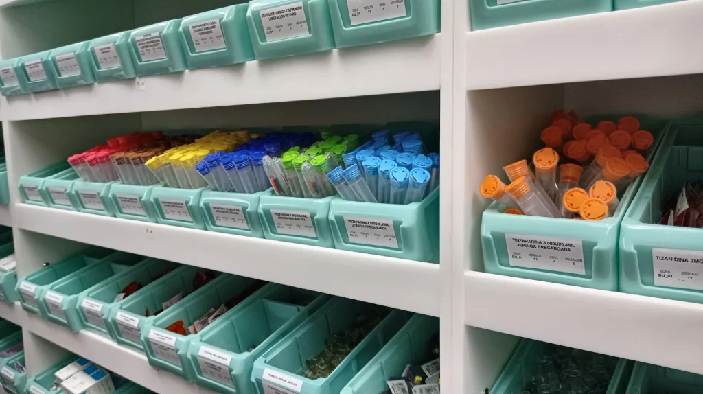 Estanterías blancas de farmacia hospitalaria con cubetas de medicación etiquetadas por módulo y nivel