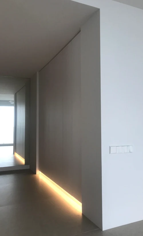 Armario empotrado de puertas lisas sin tiradores, lacado en gris claro, con tira de luz LED en el zócalo