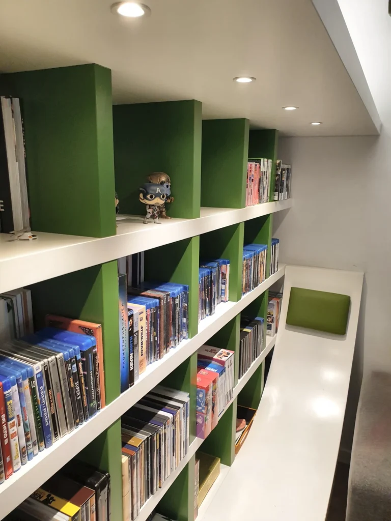 Detail of the bookcase with recessed ceiling spotlights and a curved bench with a green upholstered back