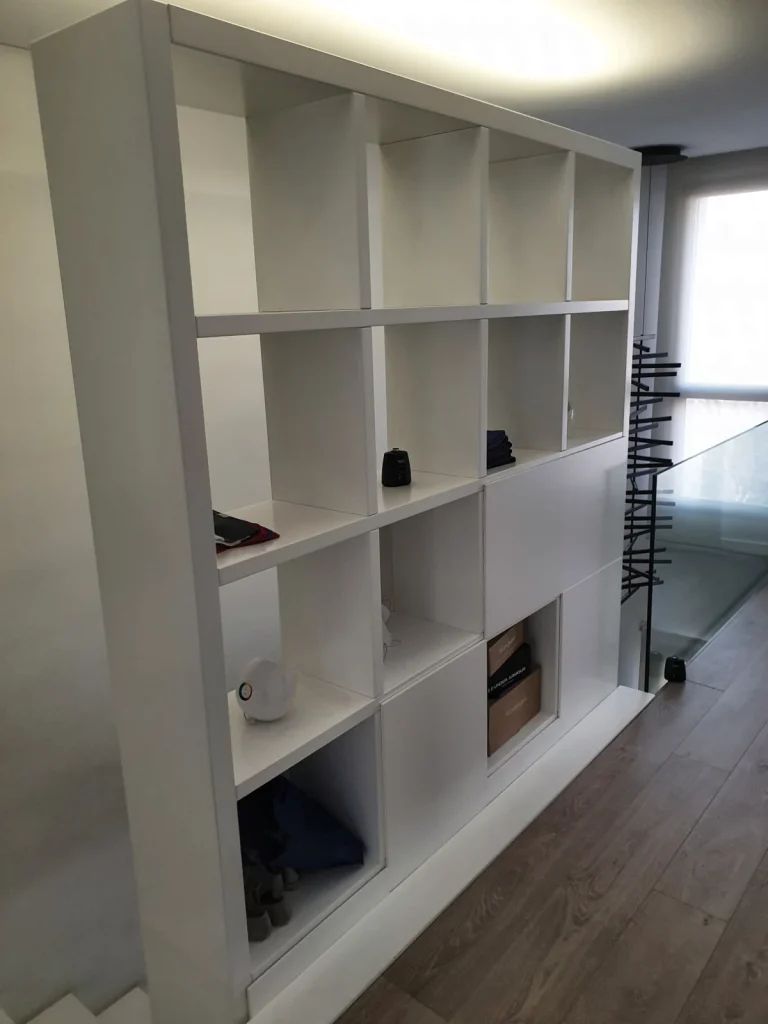 White lacquered bookcase of square modules with doors, next to the staircase of a home