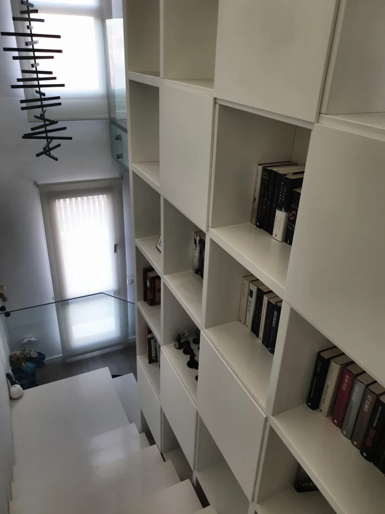 Librería lacada en blanco a doble altura a lo largo de una escalera, con huecos abiertos y puertas